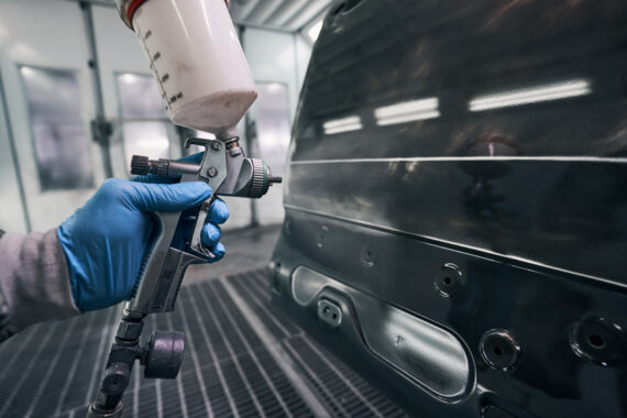 Spraying gun used for painting car in new colour Auto repair specialist spraying car panel with painting material from paint pistol in workshop